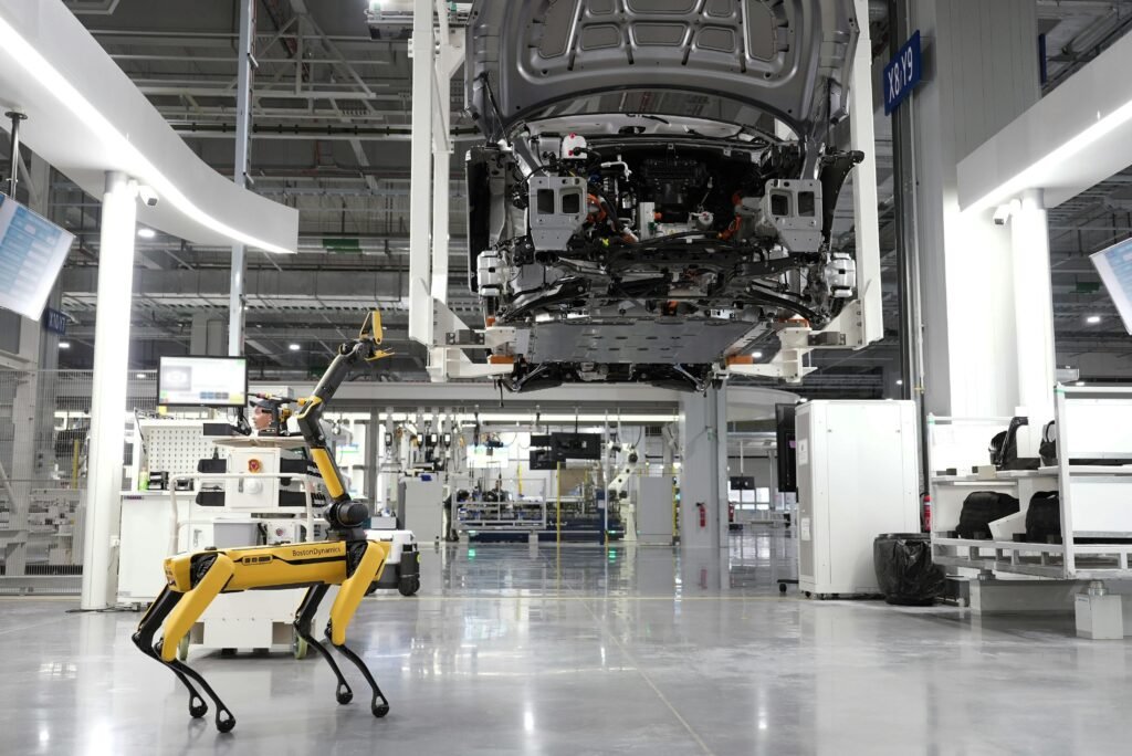 Despre noi A robotic dog oversees an automated car assembly in a high-tech factory setting.